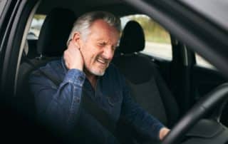 Man with whiplash sitting inside car clutching back of neck after accident